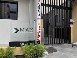 A gated entrance with a sign for 'MAX Jardim São Paulo' and a security guard post. - ELEGANCE SUÍTES MAX JARDIM (São Paulo)
