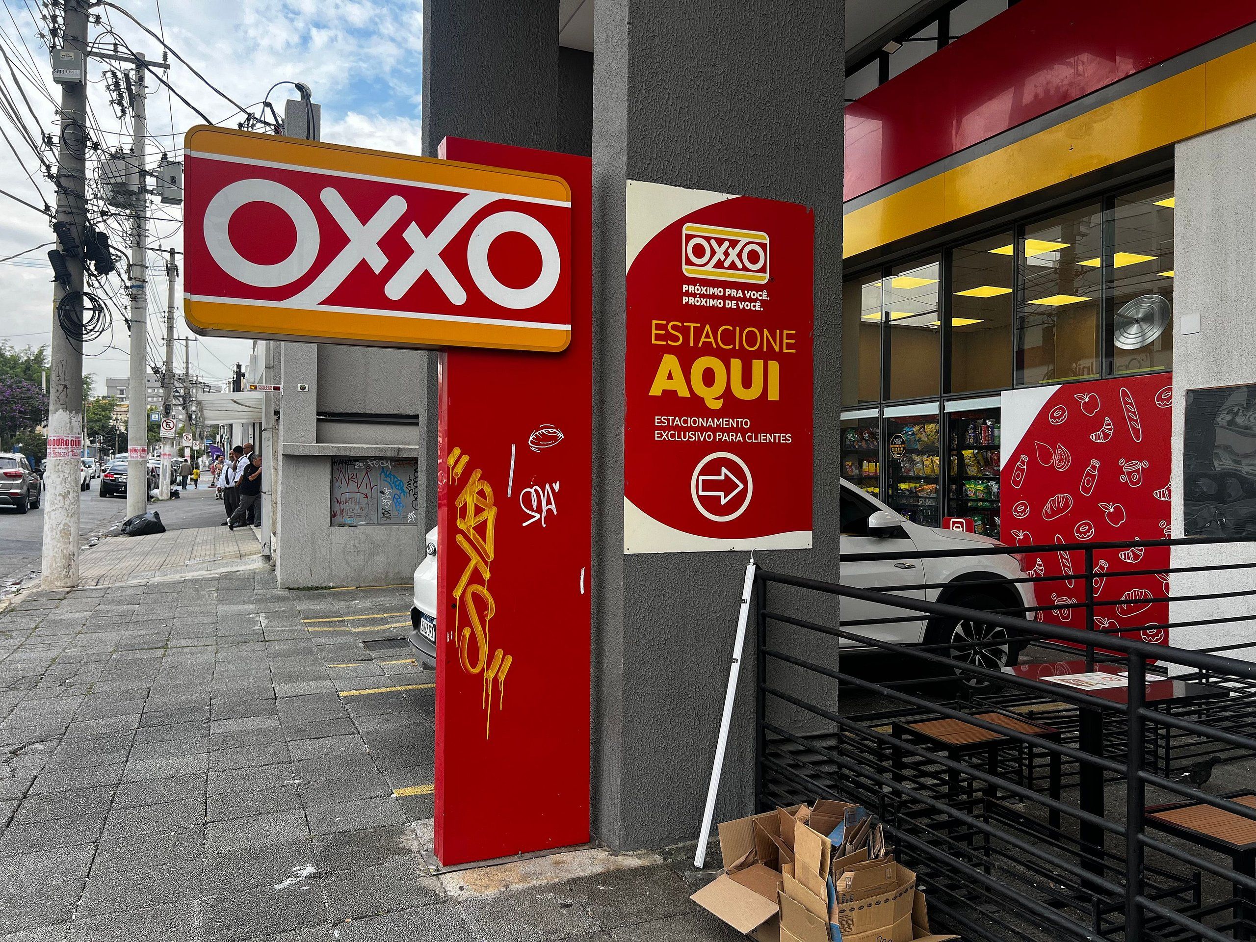 A storefront with a prominent red and yellow sign for OXXO, a food delivery service, and a sign indicating a customer service station.