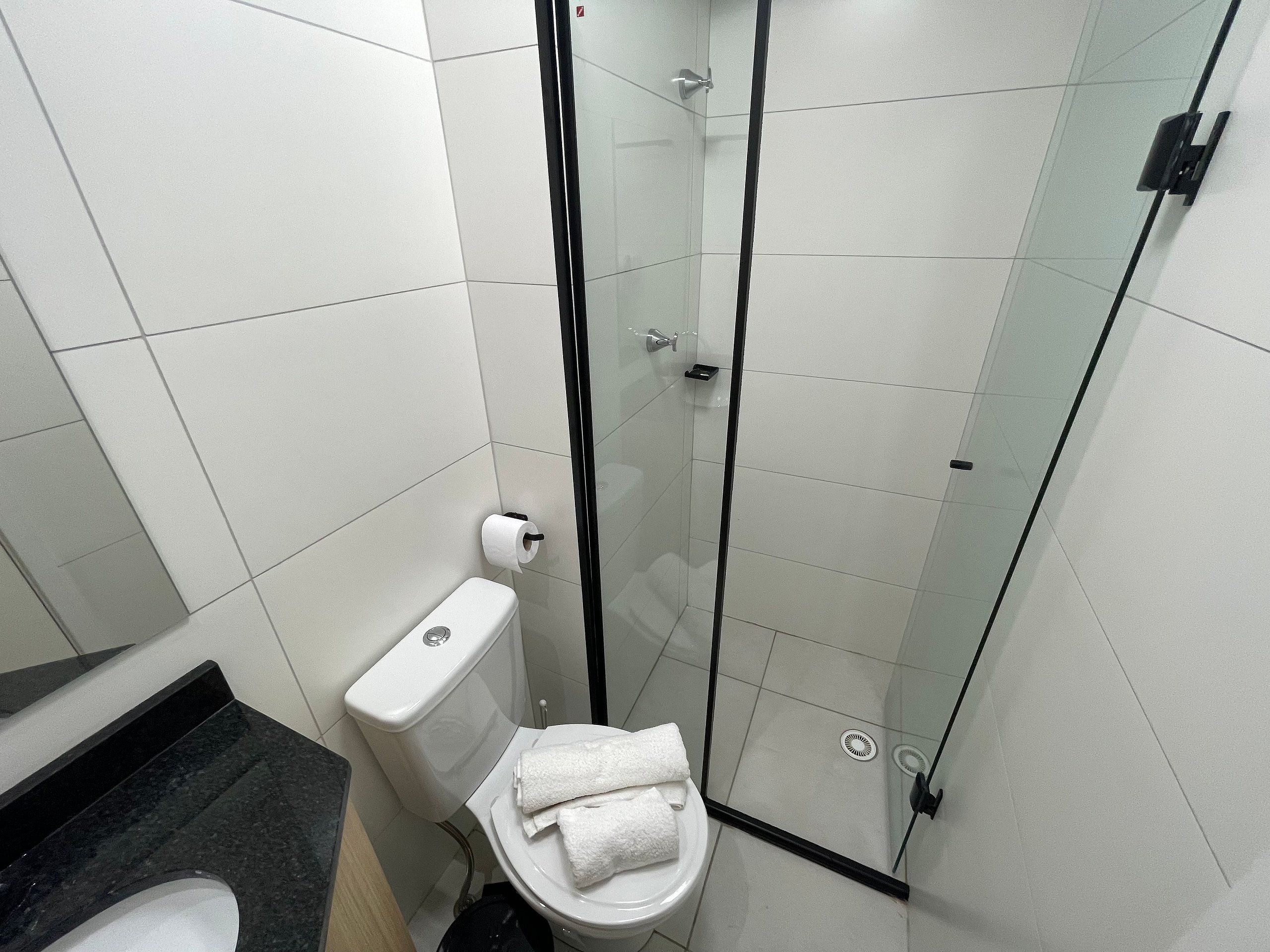 Un baño con inodoro, cabina de ducha de vidrio y encimera negra.