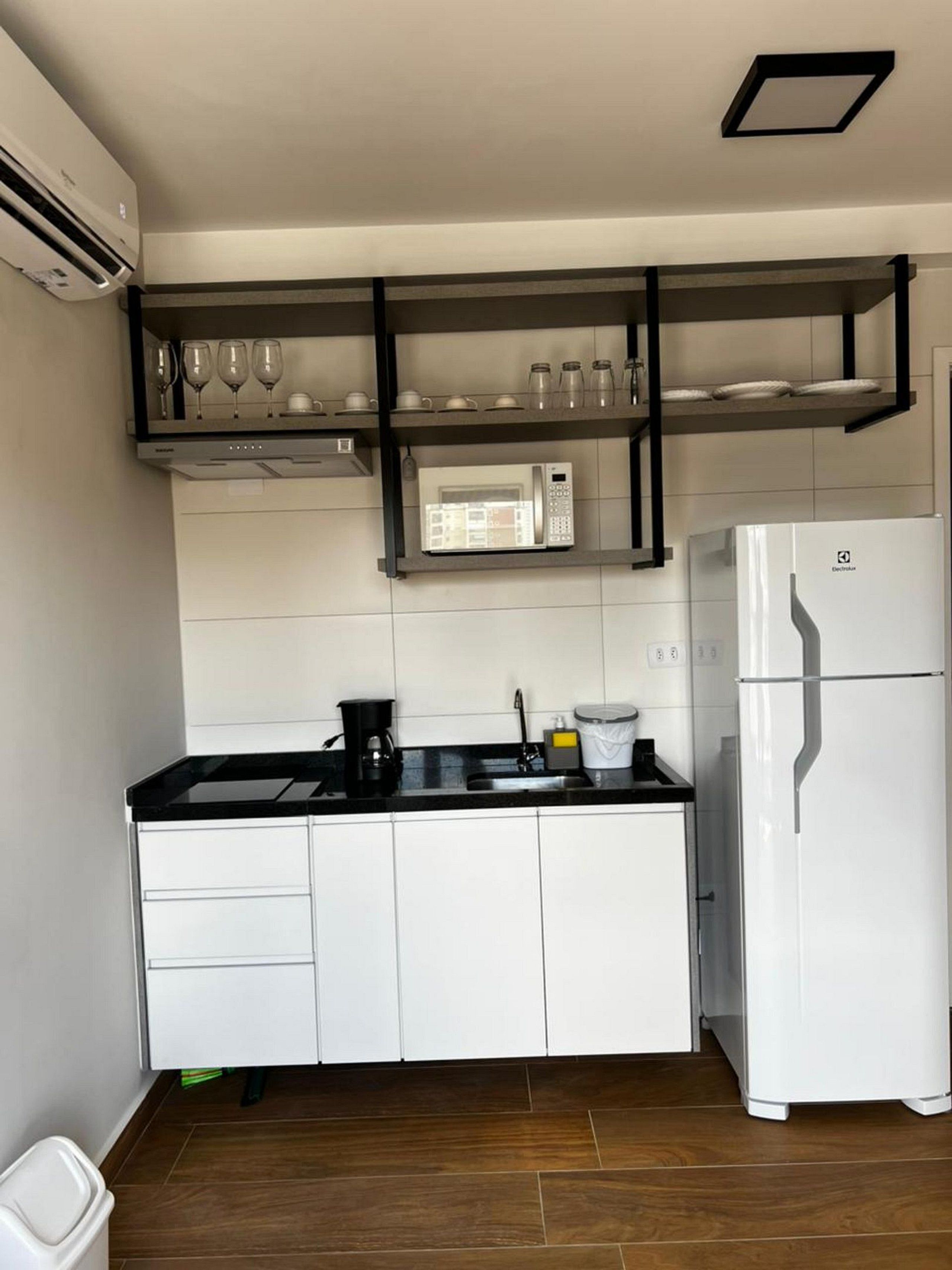 A modern kitchen with white cabinets, a black countertop, a white refrigerator, and a built-in microwave shelf.