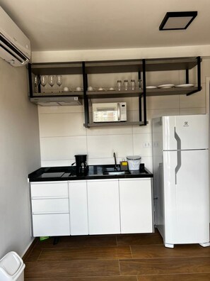Une cuisine moderne avec des armoires blanches, un plan de travail noir, un réfrigérateur blanc et une étagère intégrée pour le micro-ondes.