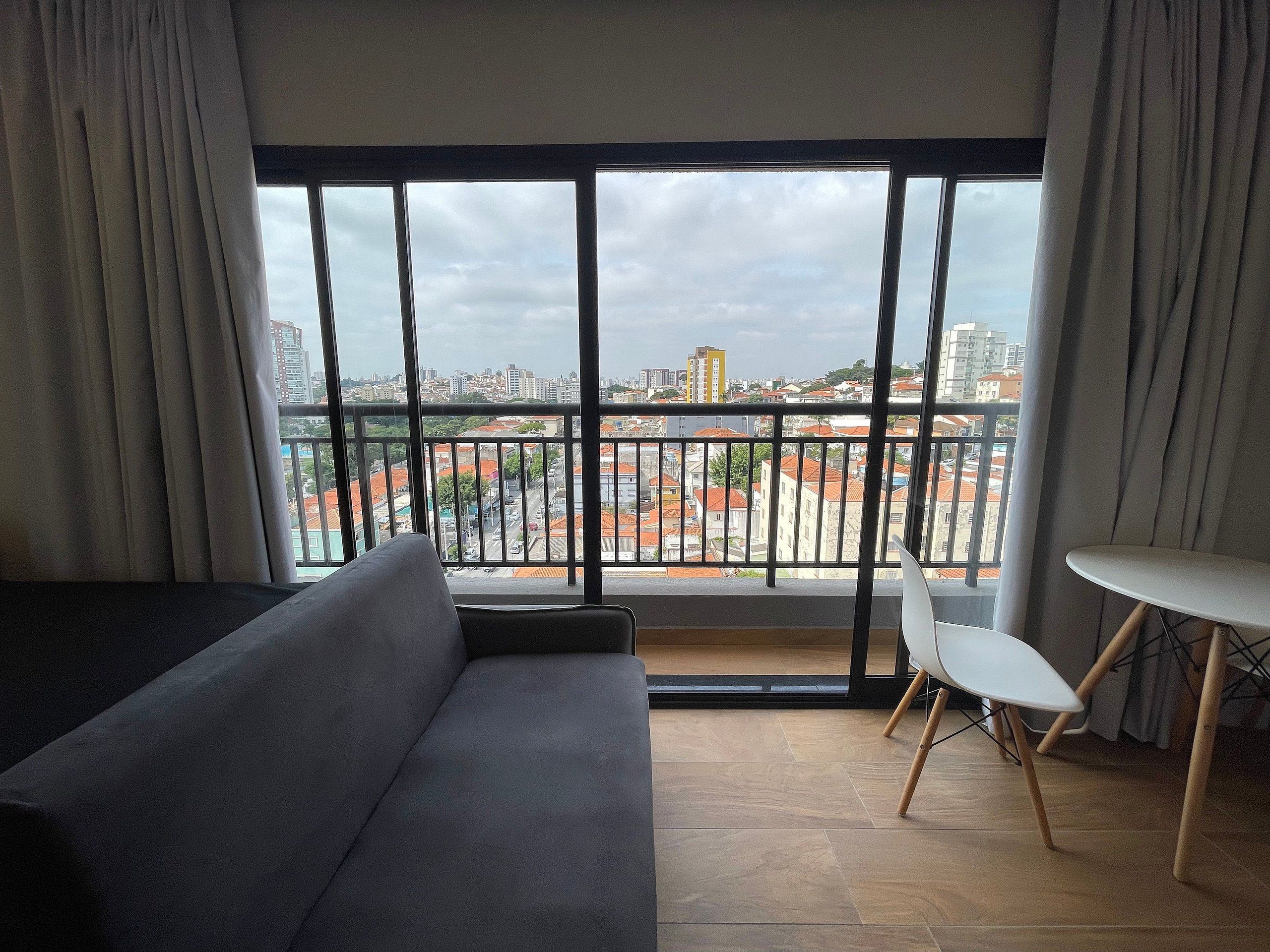 A modern living room with a large window, a sofa, a small table, and a chair.