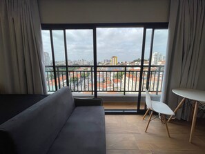 Un salon moderne avec une grande fenêtre, un canapé, une petite table et un fauteuil.