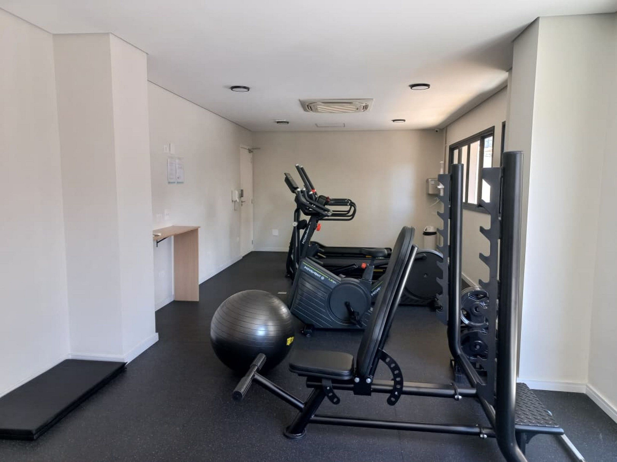 A gym with exercise equipment, a black exercise ball, and a bench.