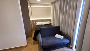 Ett hotellrum med en säng, en soffa, ett nattduksbord och ett fönster med gardiner.