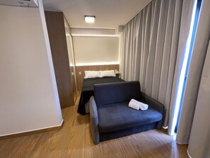 Et hotelværelse med seng, sofa, et natbord og et vindue med gardiner.