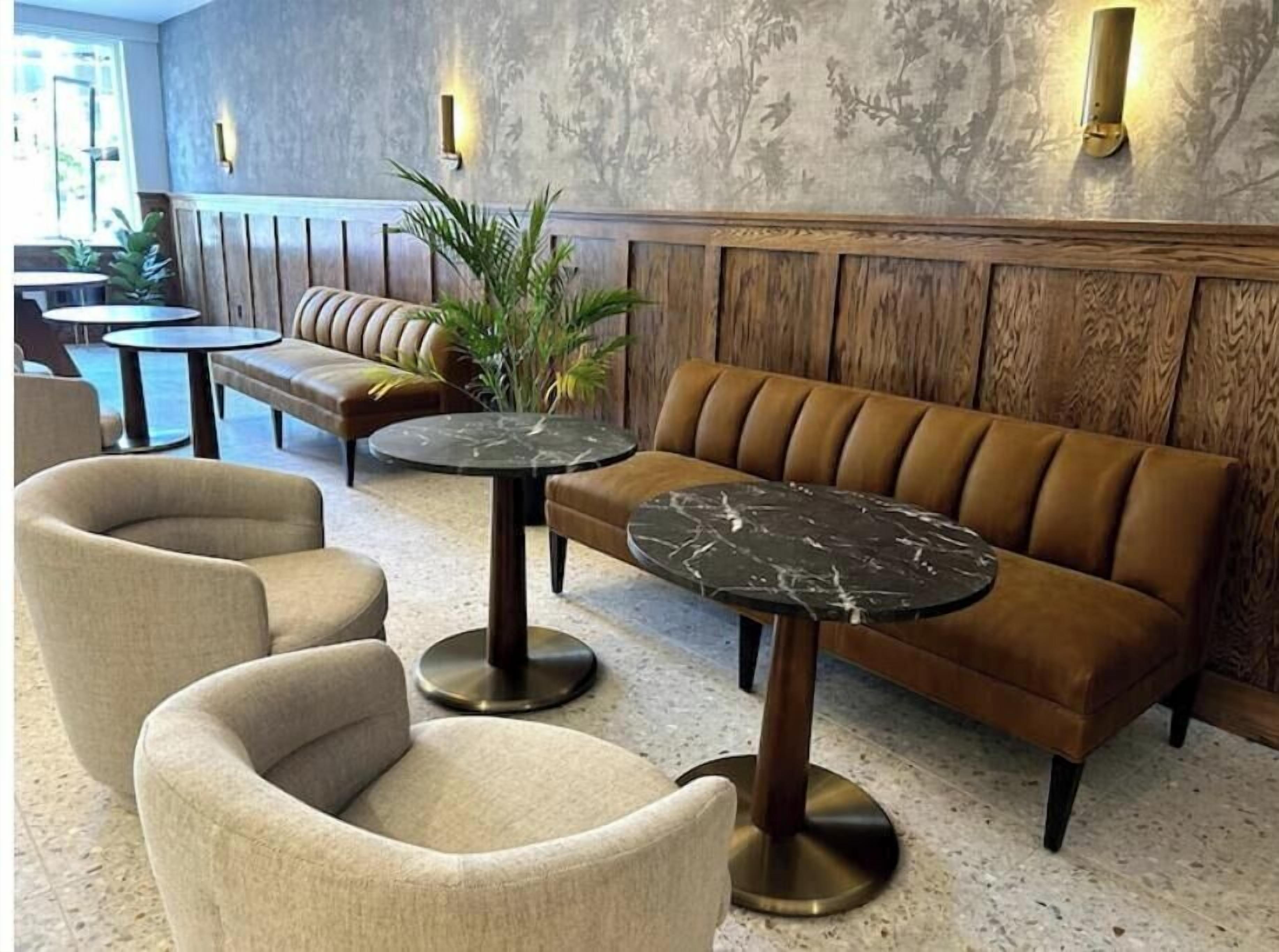 Een zithoek met een bruine bank, twee ronde tafels en beige fauteuils.