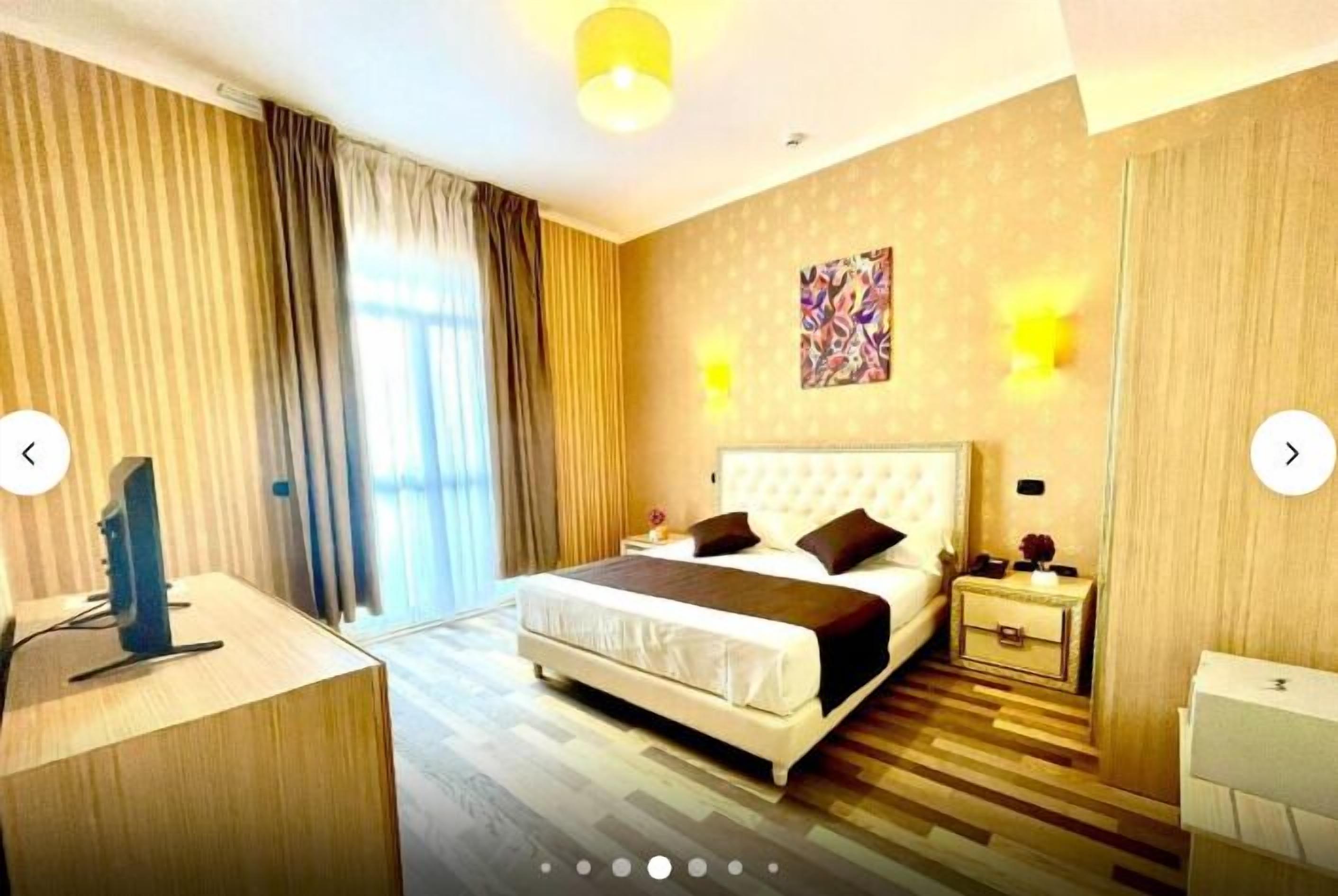 Una habitación de hotel con una cama grande, mesitas de noche, un escritorio y un espejo.