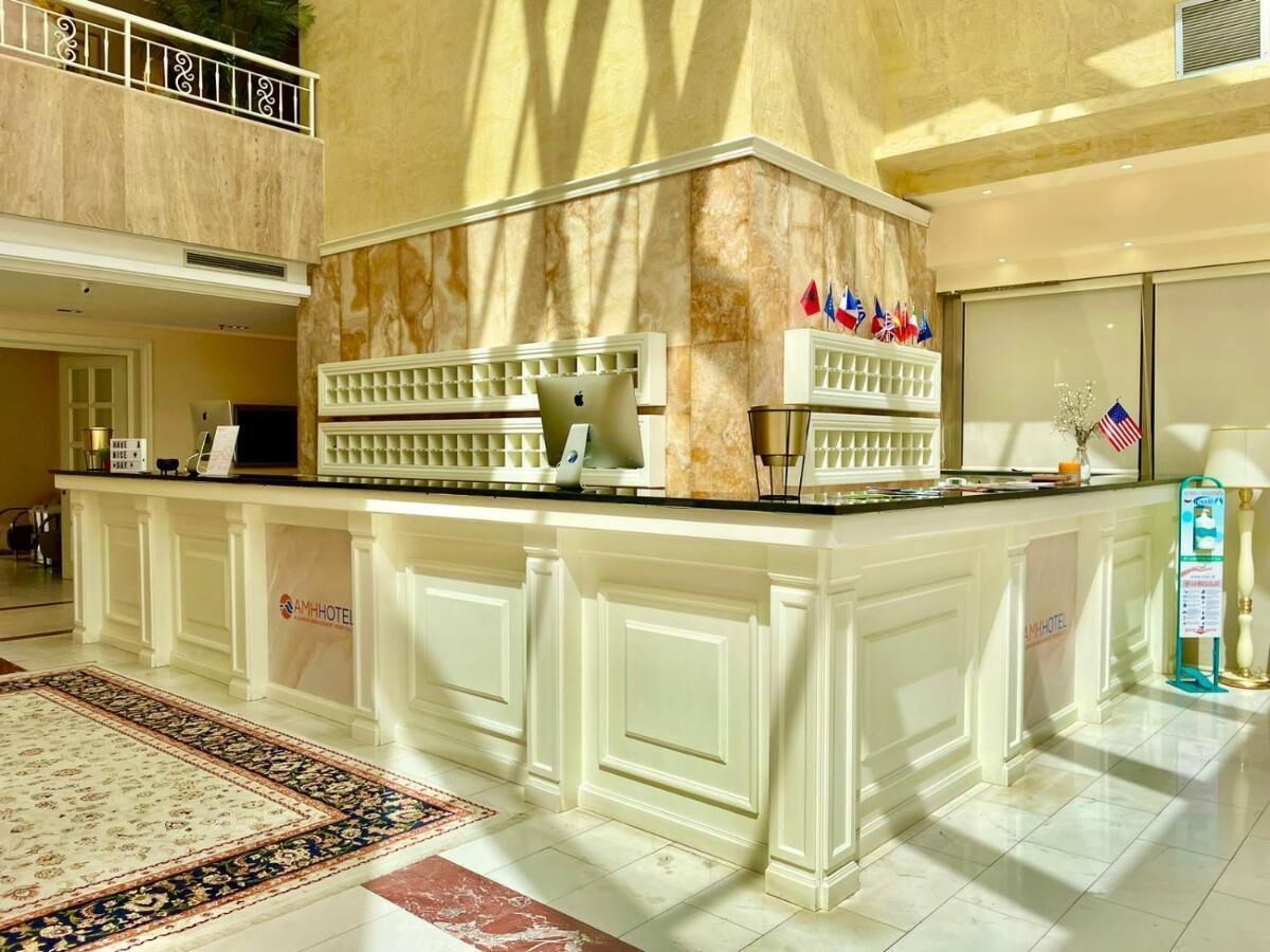 A hotel lobby with a marble reception desk, a large rug, and a sign indicating the hotel name.