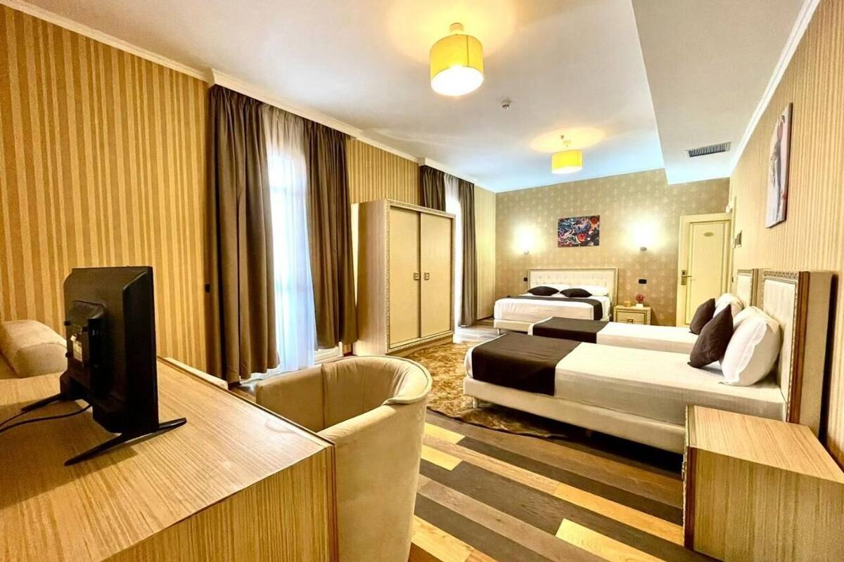 Hotellihuone, jossa on sänky, työpöytä, jossa on televisio, tuoli, vaatekaappi sekä kylpyhuone, jossa on peili ja pesuallas.