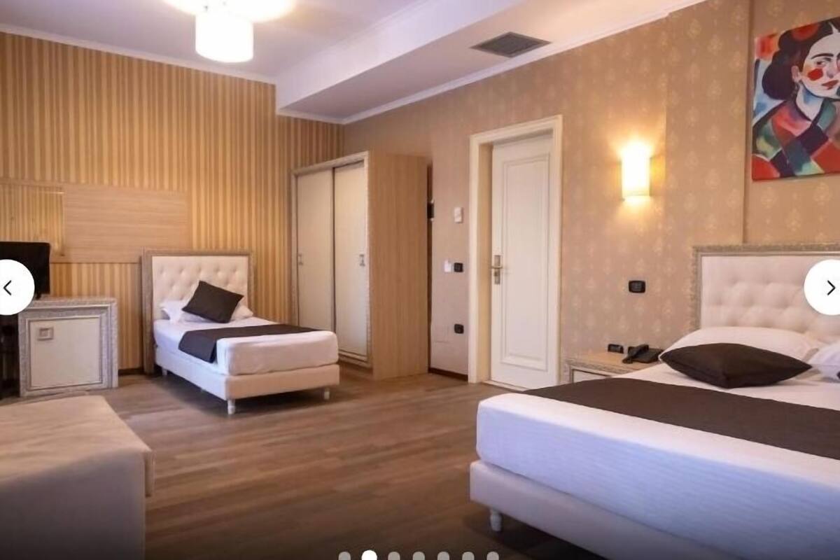 Hotellihuone, jossa on kaksi sänkyä, yöpöytä, seinävalaisin ja taulu.