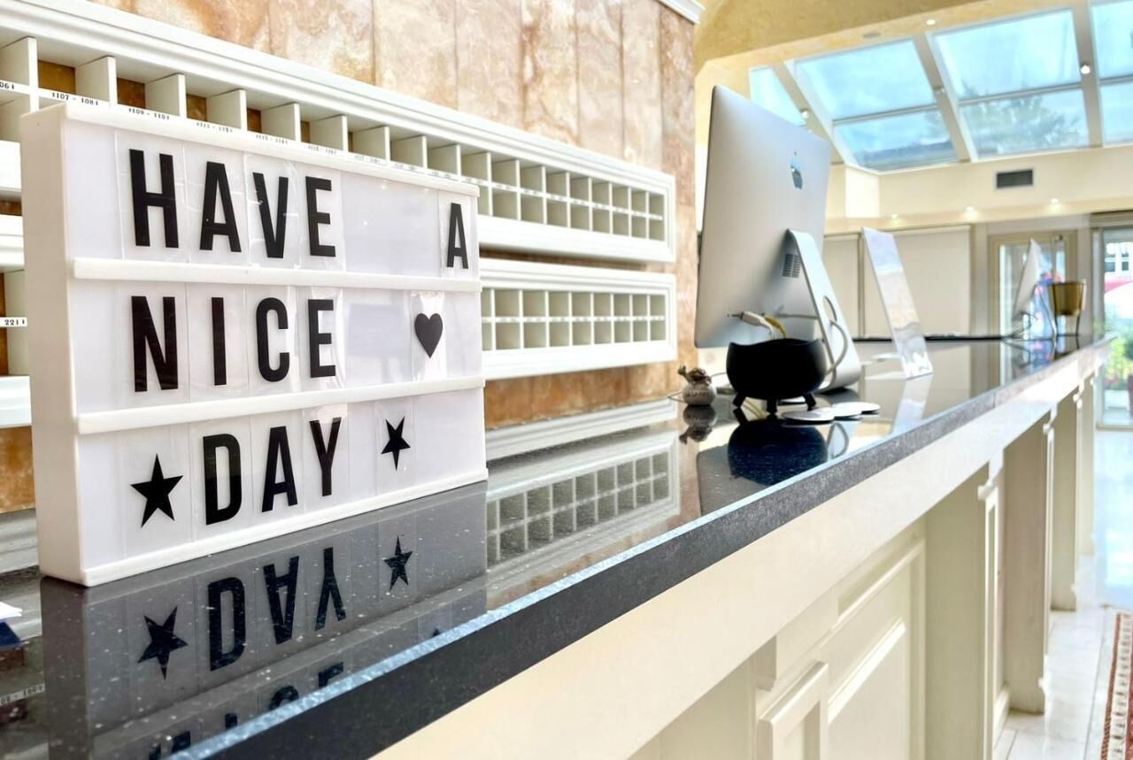 A hotel reception area with a lightbox displaying "HAVE A NICE DAY" and a desktop computer on the counter.