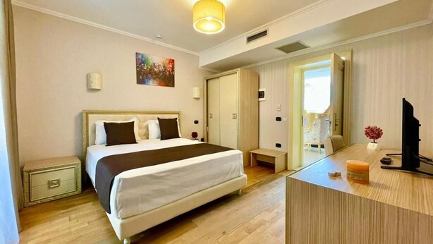 Ein Hotelzimmer mit einem großen Bett, Nachttischen, einem Schreibtisch mit Computer und einem Spiegel.
