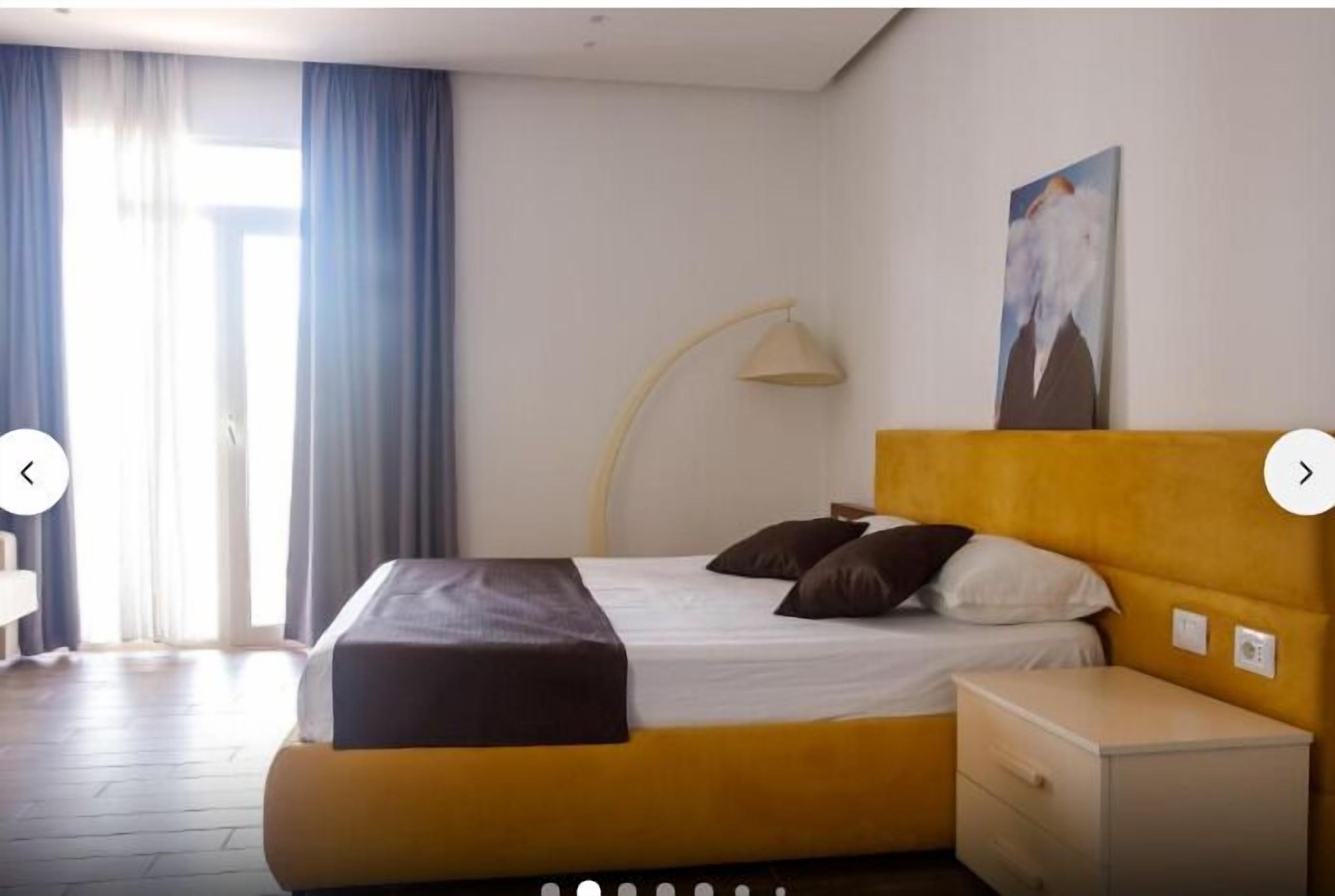 A hotel room with a bed, a nightstand, a lamp, and a painting on the wall.