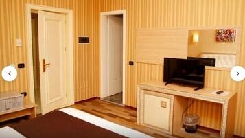A hotel room with a bed, a desk with a television, a small cabinet, and a trash bin.