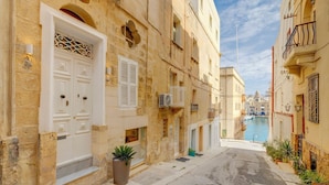 Une rue étroite bordée de bâtiments traditionnels, une porte blanche et un pot de fleurs.