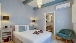 Une chambre à coucher avec un grand lit, des lampes de chevet, un fauteuil vert et une salle de bain avec un miroir et un lavabo.
