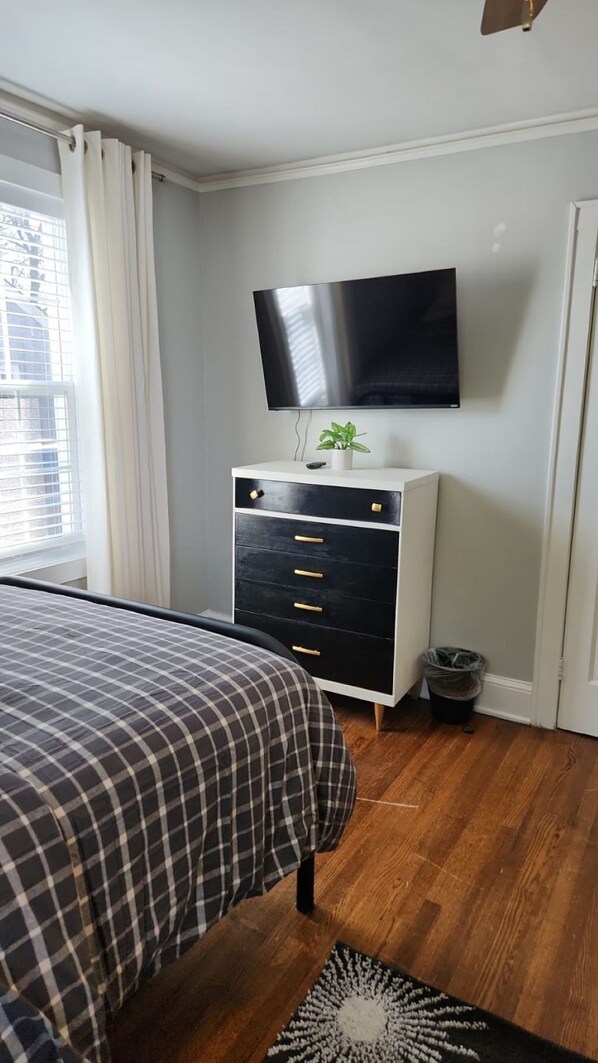 A bedroom with a bed, a dresser, a television, and a window with curtains.