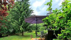 Un terrazzo in legno con tavolo e sedie, immerso nel verde e alberi.