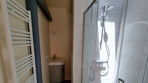 Un bagno moderno con cabina doccia in vetro, lavandino bianco e pavimento in legno.