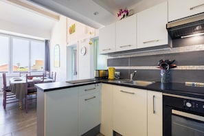 A modern kitchen with white and black cabinetry, a built-in oven, and a dining area with a table and chairs.