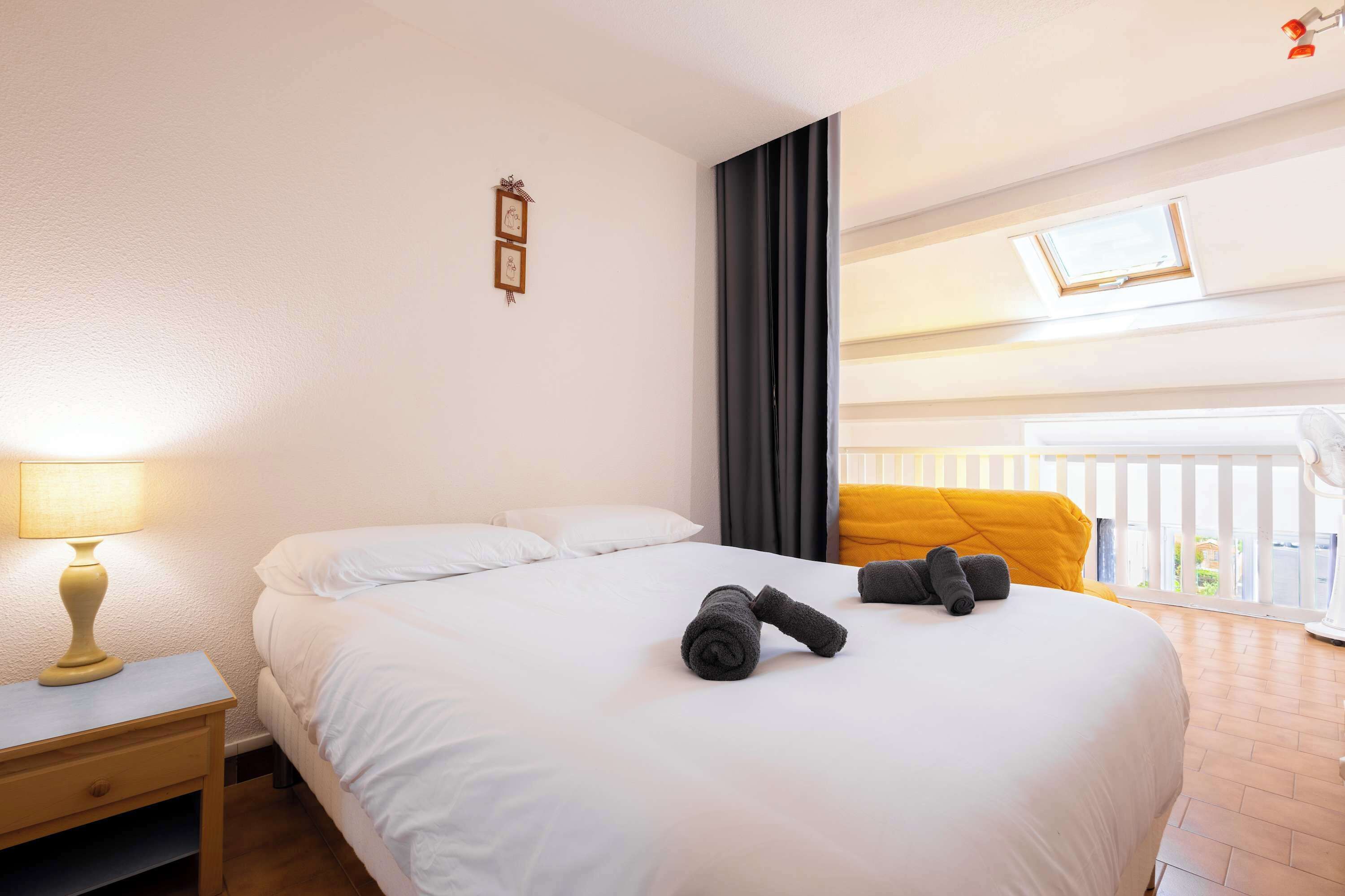 A hotel room with a bed, a nightstand, a lamp, a window with curtains, and a balcony view.
