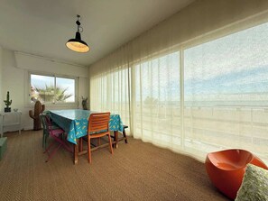 Un comedor con mesa y sillas, un colgador de luces y vistas al mar a través de amplios ventanales.