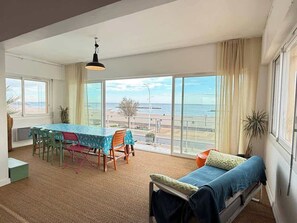 A room with a large window overlooking a beach, a dining table with chairs, a bed, and a hanging light fixture. - Spacious 120 m² Seafront Apartment (Valras-Plage)