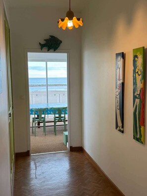 Un pasillo con piso de madera, vista al mar a través de un ventanal y dos obras de arte en la pared.