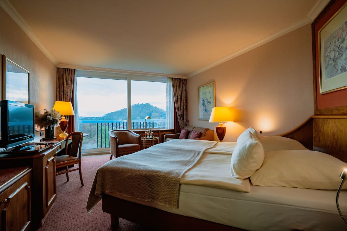 Habitación de hotel con cama, escritorio, silla, lámparas y vistas a la montaña.