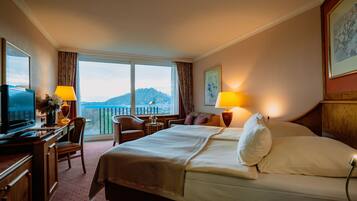Habitación de hotel con cama, escritorio, silla, lámparas y vistas a la montaña.