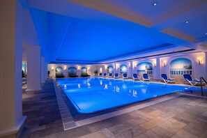 Una piscina interior con iluminación azul, asientos hundidos y suelo de baldosas.