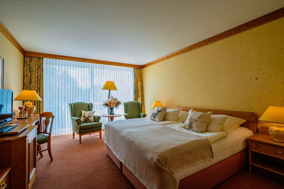Una habitación de hotel con una cama grande, dos sillas, un escritorio y una lámpara.