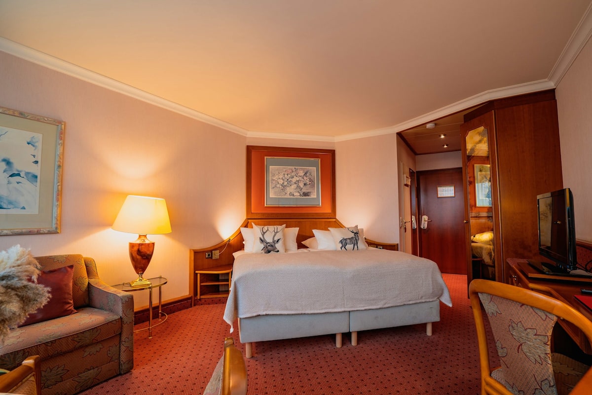 Una habitación de hotel con cama, escritorio, silla, lámpara y televisor.