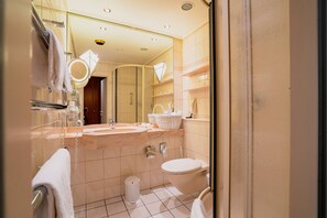 Un baño con ducha de vidrio, inodoro blanco, lavamanos con espejo y perchero para toallas.