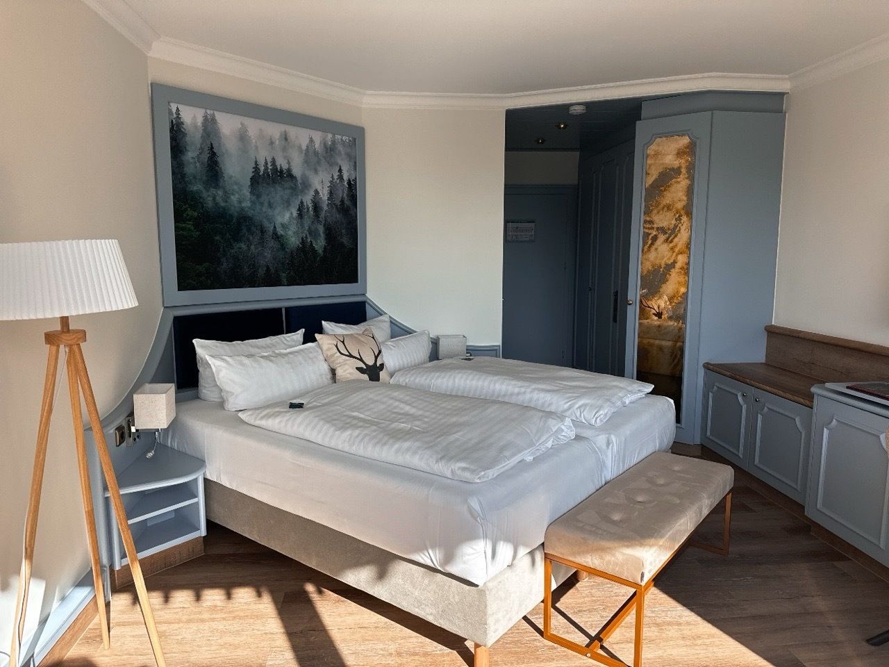 Un dormitorio con una cama grande, mesitas de noche, un banco y un cuadro en la pared.