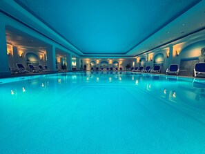 Una piscina interior amplia con numerosas tumbonas dispuestas alrededor del borde.