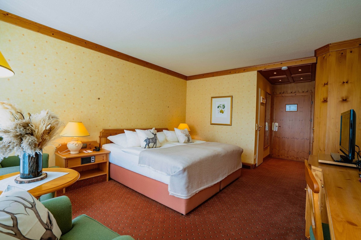 Una habitación de hotel con cama, mesita de noche, lámpara, silla, mesa y televisión.