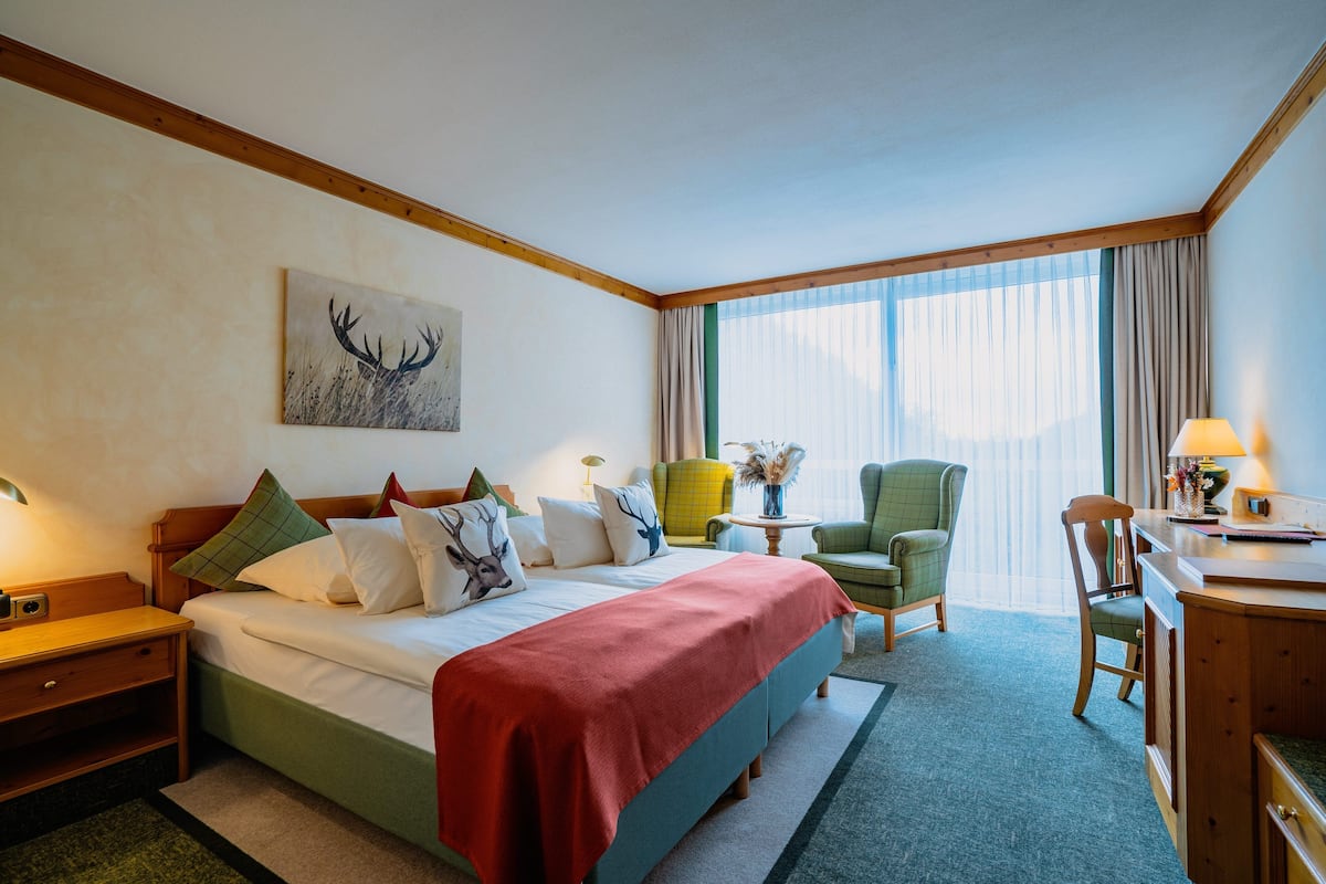 Una habitación de hotel con una cama grande, un escritorio, una silla y una ventana con cortinas.