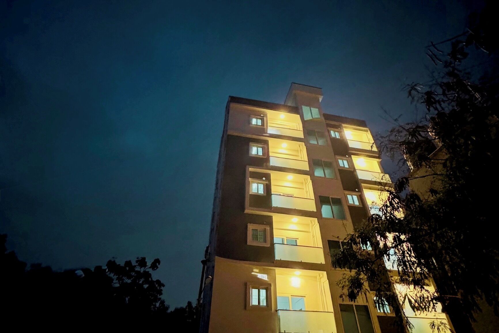 Um edifício com vários andares, janelas iluminadas e varandas à noite.