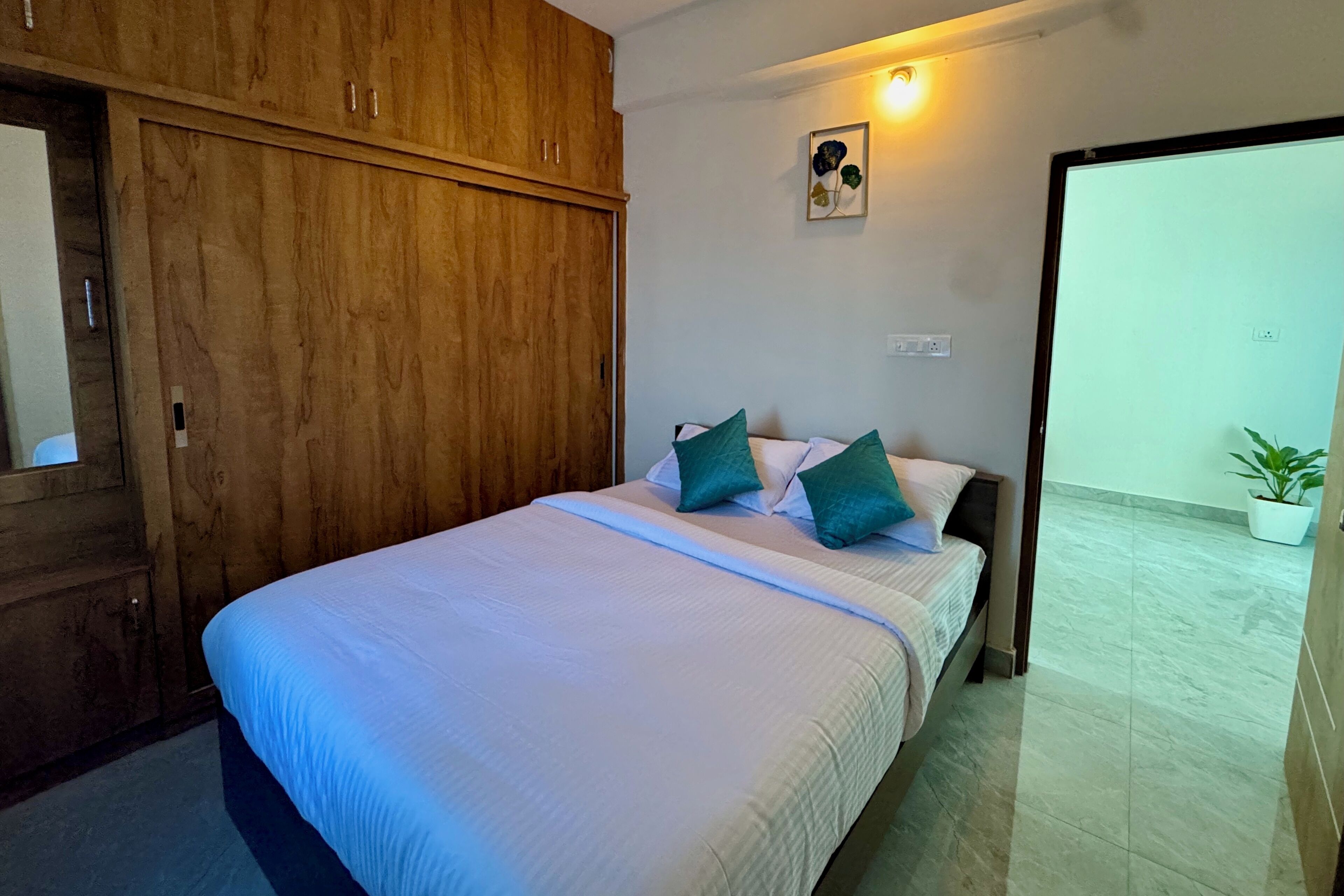 A bedroom with a bed, wooden wardrobe, and a potted plant.