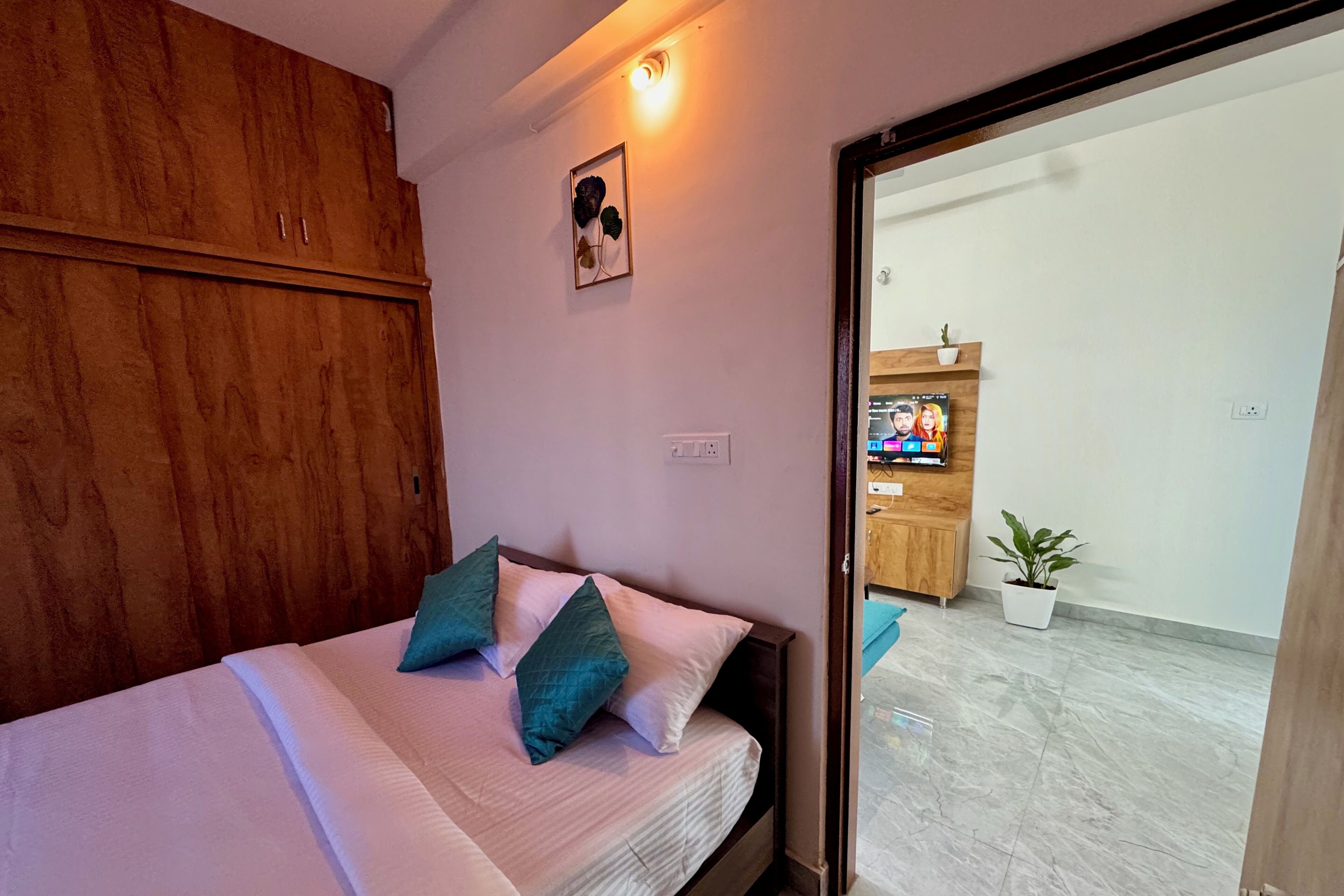 A bedroom with a bed, wooden wardrobe, and a small potted plant.