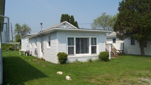 A single-story house with a front porch, a small front yard, and a visible chimney. - Charming 1-bedroom cottage in beautiful Narragansett with AC, WiFi (Narragansett)