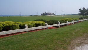 A golf course with a white fence, manicured bushes, and a distant building. - Charming 1-bedroom cottage in beautiful Narragansett with AC, WiFi (Narragansett)