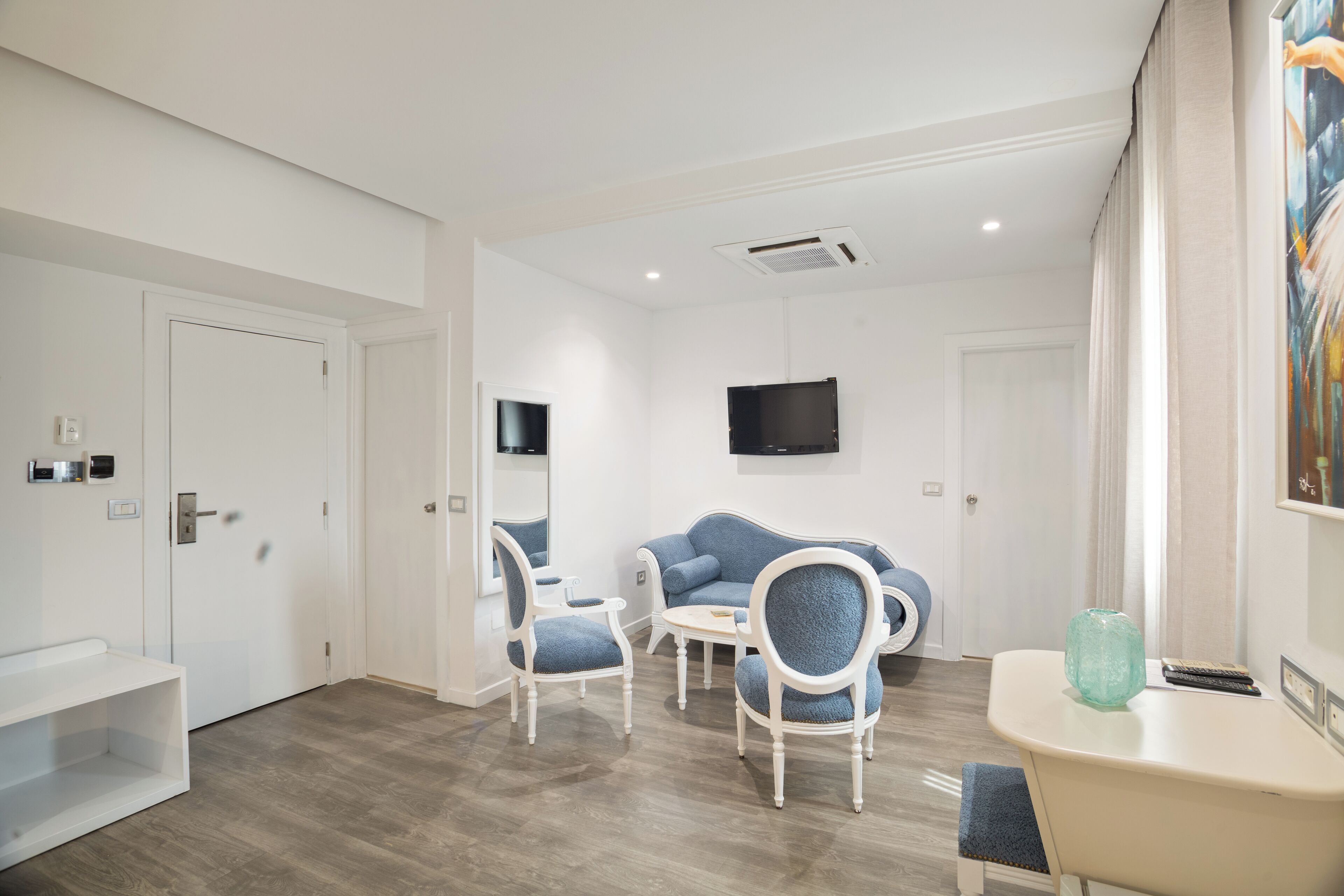 A modern hotel room with a seating area, a flat-screen TV, and a painting on the wall.