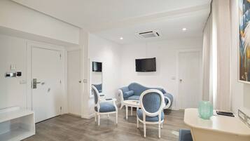 A modern hotel room with a seating area, a flat-screen TV, and a painting on the wall.