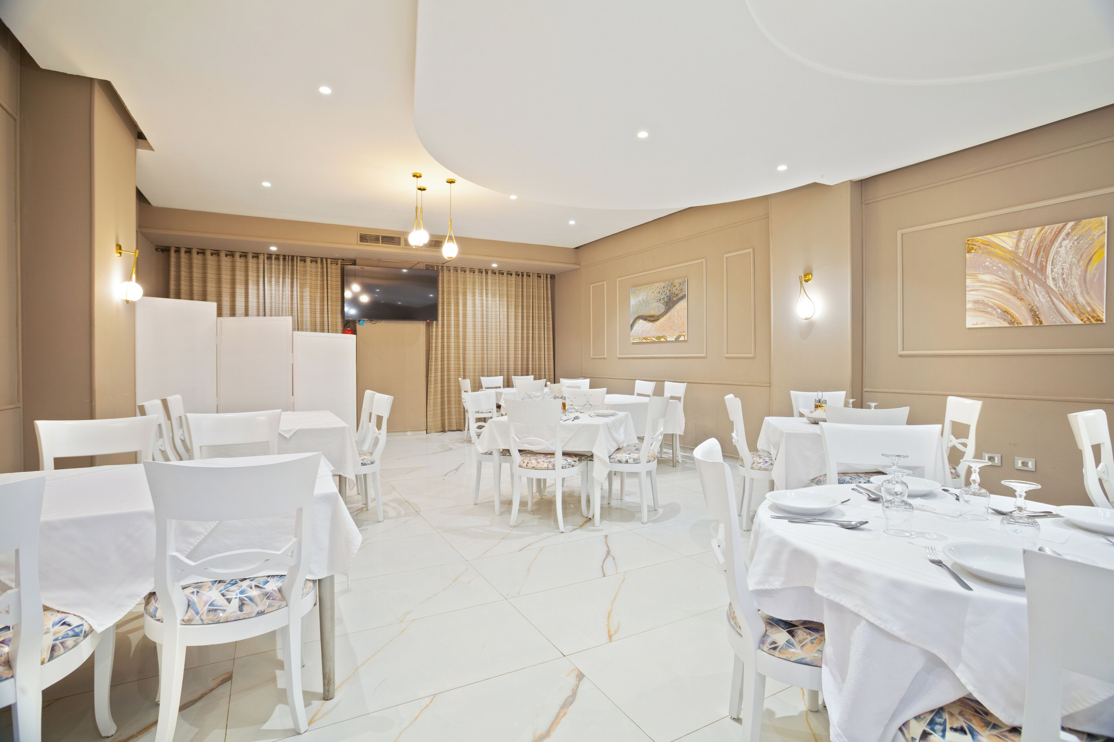 A spacious dining area with white tables and chairs, a flat-screen TV mounted on the wall, and a large abstract painting on the wall.