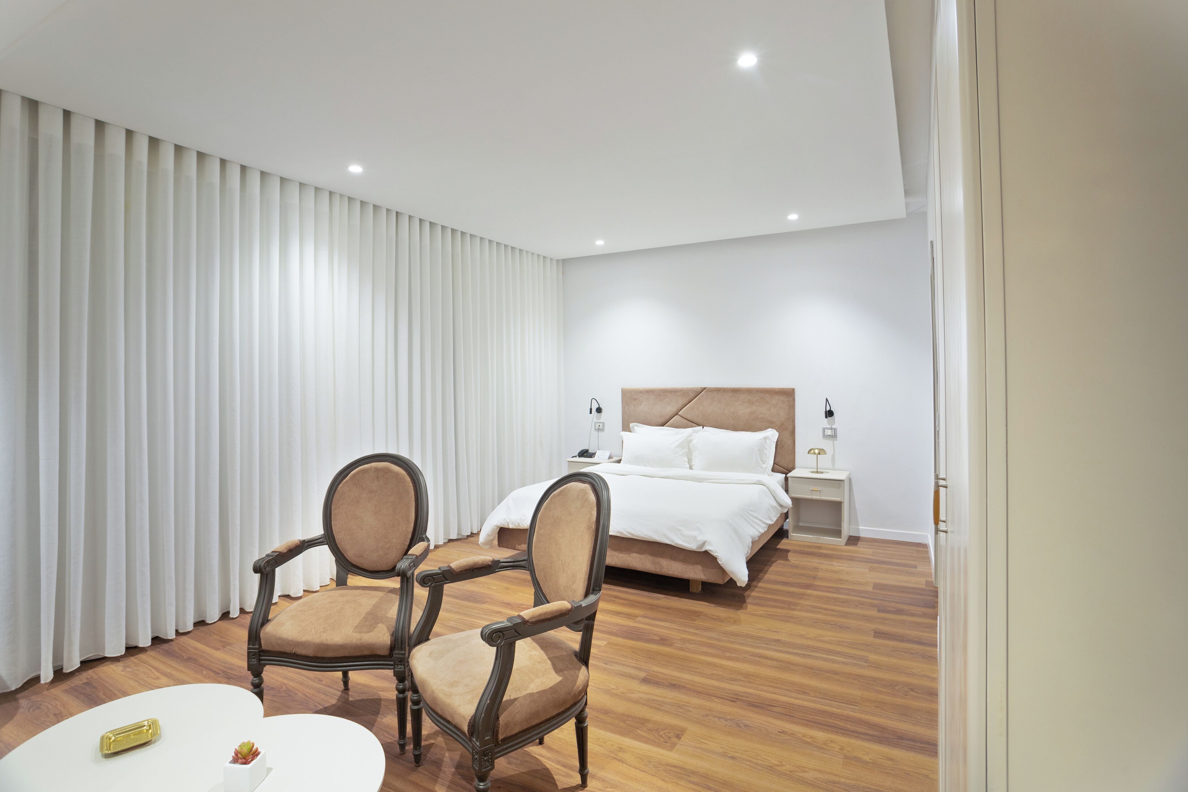 Una habitación de hotel con cama, dos sillones, una mesita y una mesita de noche.