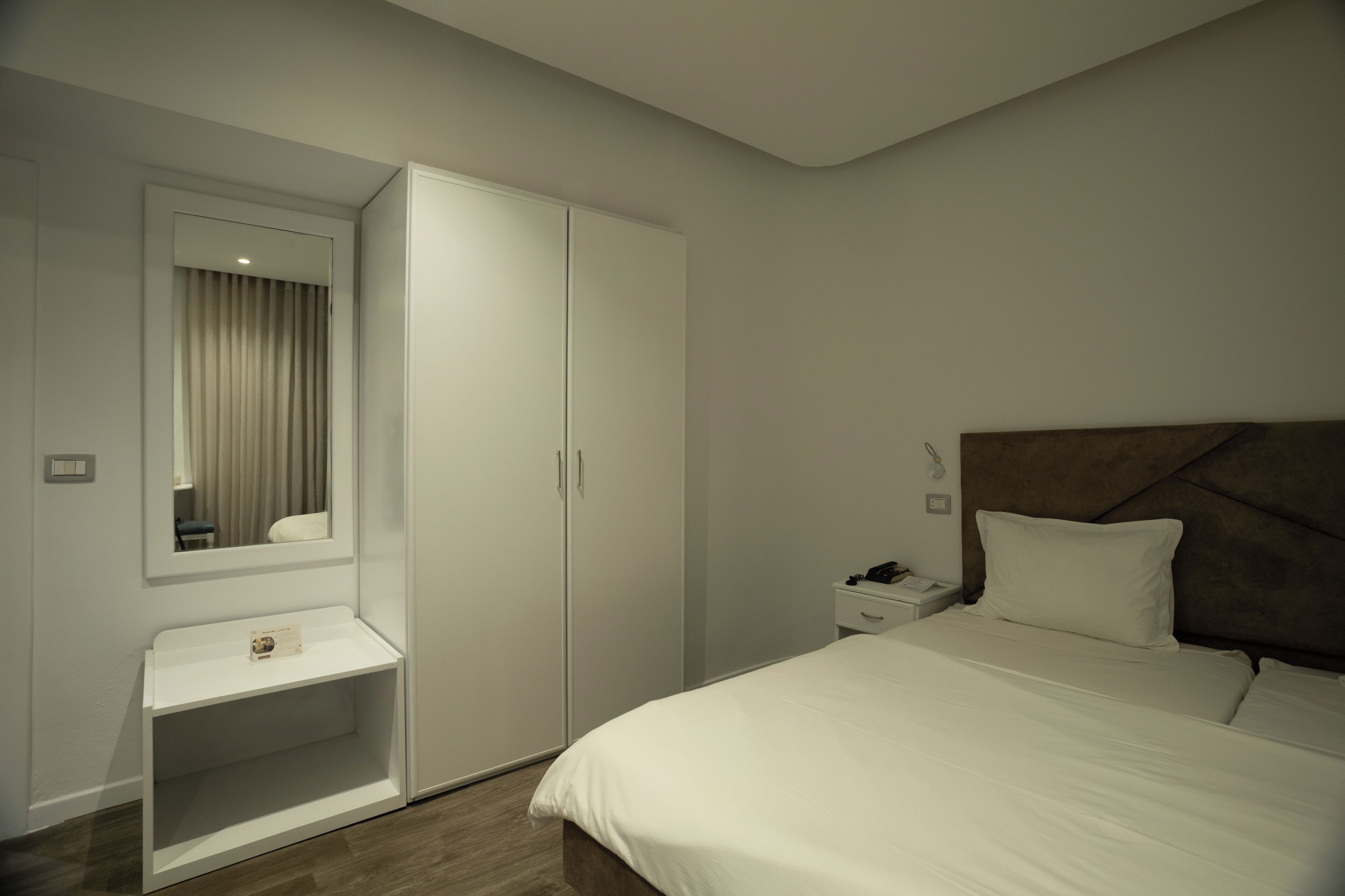 A bedroom with a bed, a nightstand, a wardrobe, a mirror, and a shelf.