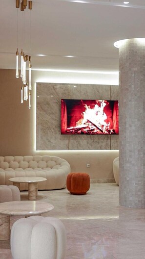Ein modernes Wohnzimmer mit einem großen Flachbildfernseher, einem beigefarbenen Sofa, einem runden Couchtisch und einem außergewöhnlichen orangefarbenen Hocker.